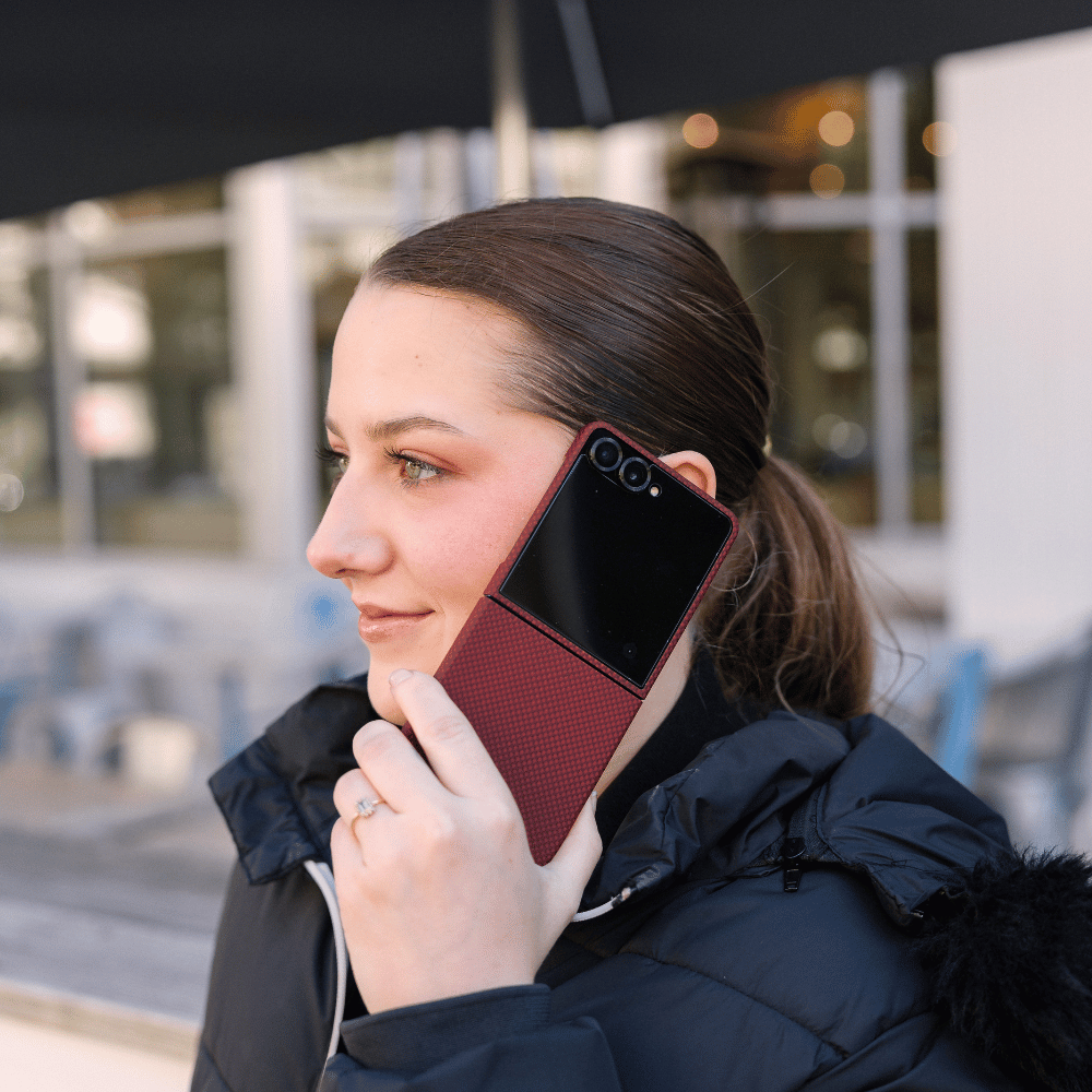 Lifestyle shot of a woman holding Samsung Galaxy Z Flip 8 with crimson red carbon fiber textured magnetic phone case outdoors, real street scene daily use photo of foldable flip phone MagSafe cover