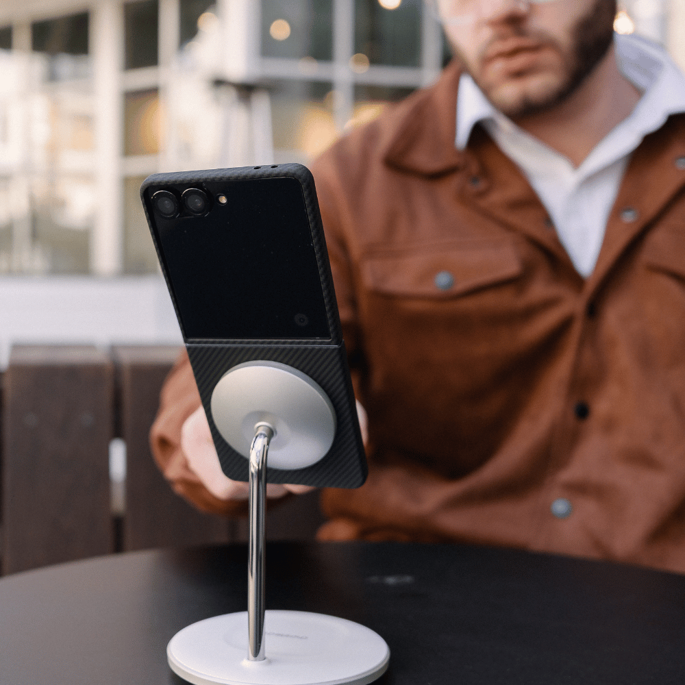 galaxy z flip 7 wit aramid fiber case attached to magsafe stand. A man in a brown jacket is blurred in the background at an outdoor table.