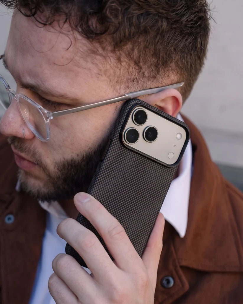 Man holding iPhone 18 Pro Max with Thinborne brown checkered aramid fiber case to ear for call, street lifestyle shot