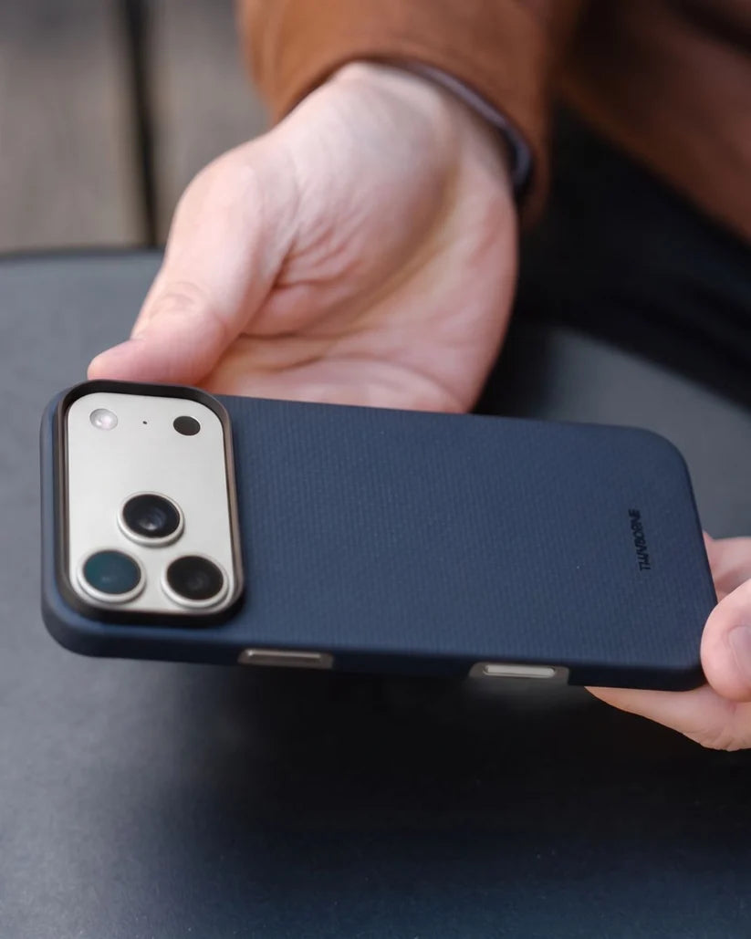 Two hands flipping iPhone 18 Pro Max with Thinborne navy aramid fiber case, showing full back texture and camera cutout