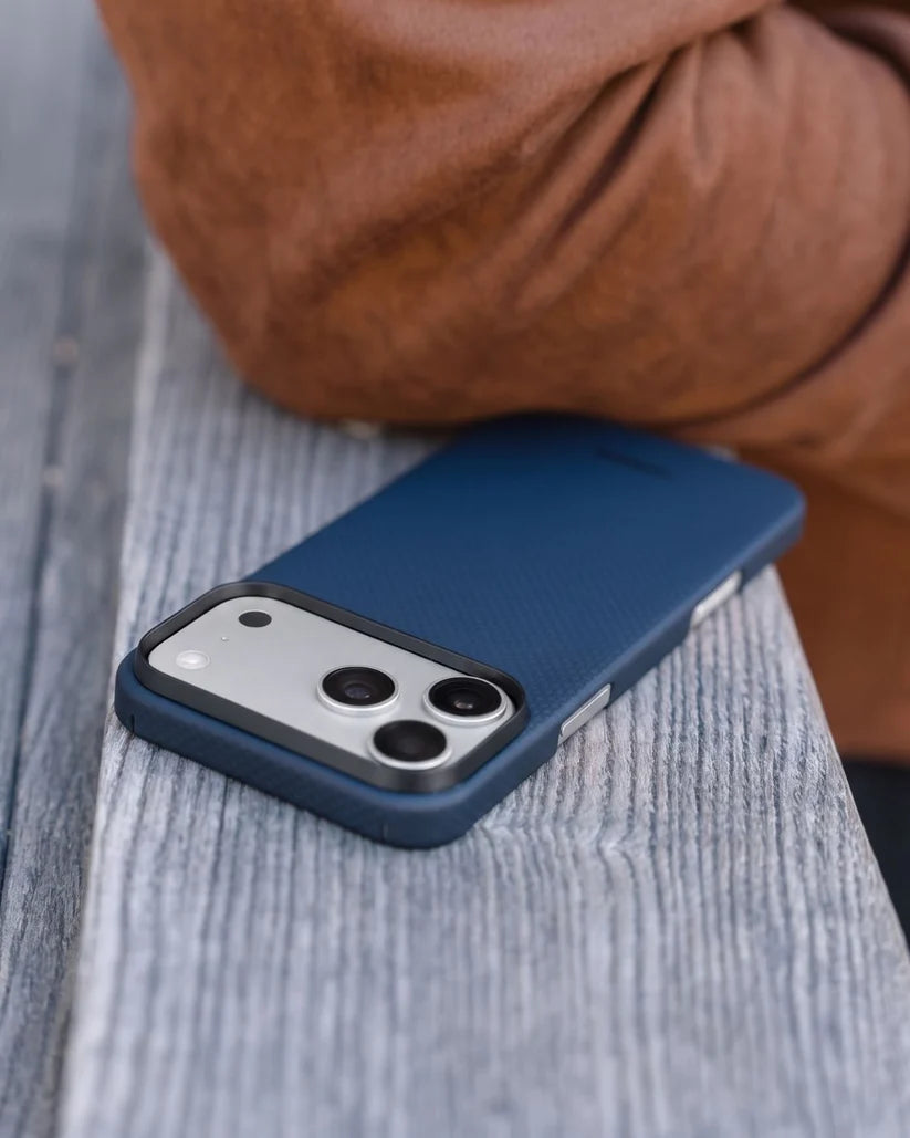 Thinborne navy aramid fiber iPhone 18 Pro Max case resting on wooden bench, outdoor lifestyle side shot
