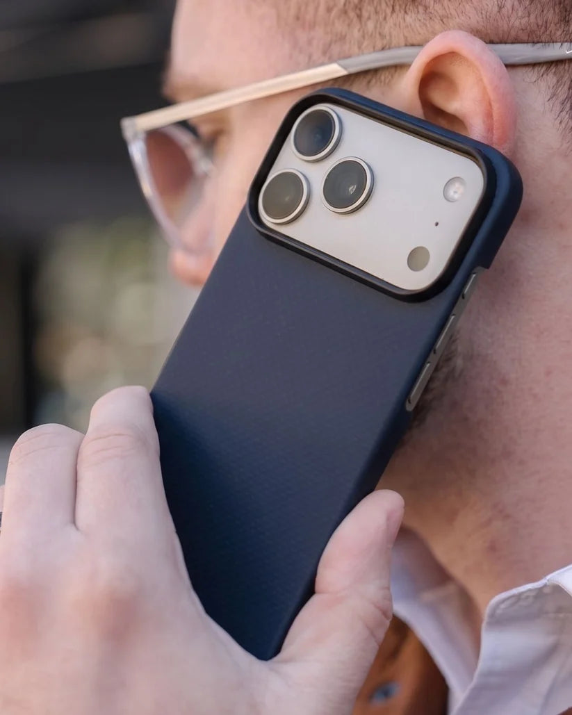 Man holding iPhone 18 Pro Max with Thinborne navy aramid fiber case to ear, outdoor lifestyle phone call shot