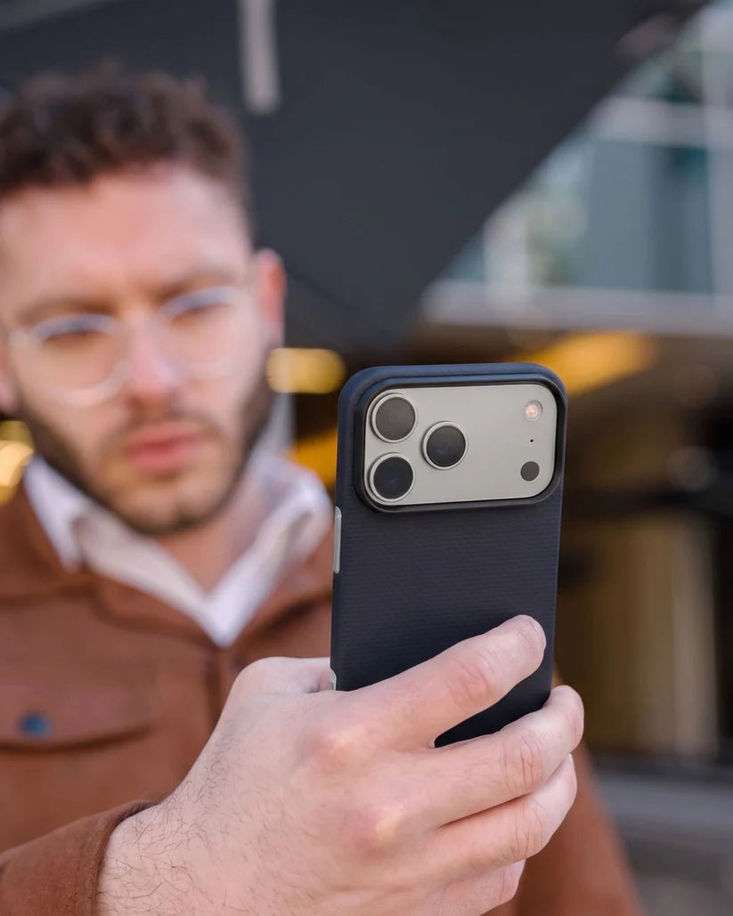 Man holding iPhone 18 Pro Max fitted with Thinborne navy aramid fiber protective case, outdoor street lifestyle photo